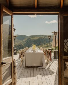 an open door leading to a table with white cloths on it and mountains in the background