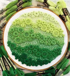 a close up of a embroidery on a table with green thread and needles next to it