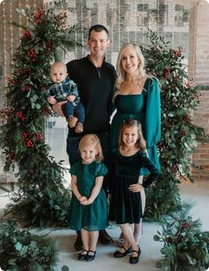 a man and woman with two children standing in front of a christmas wreath