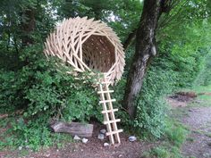 a sculpture made out of bamboo sticks in the grass next to a tree and some rocks