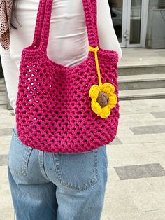 a woman holding a pink crocheted bag with a yellow flower on the front