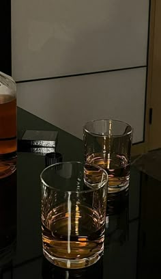 two glasses sitting on top of a black table next to a bottle and glass container