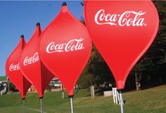 three large coca - cola balloons sitting in the grass