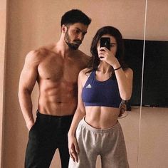 a man standing next to a woman taking a selfie in front of a mirror