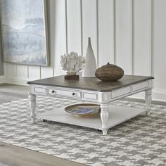 a white coffee table sitting on top of a rug next to a vase filled with flowers