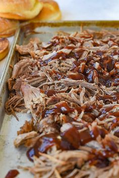 barbecued pork with bbq sauce on a baking sheet next to sliced bagels