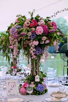 a tall vase filled with pink and purple flowers on top of a white table cloth