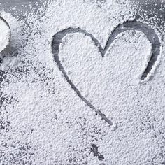 a heart drawn in the snow next to two spoons and some powdered sugar