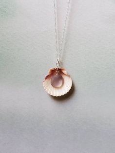 a necklace with a pink shell hanging from it's side on a gray surface