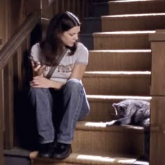 a woman sitting on the stairs next to a cat with her hand on her chest