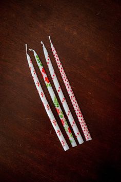 three white candles with red and green designs on them sitting on a table next to each other