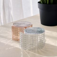 two rolls of silver and gold colored paper on a table next to a potted plant