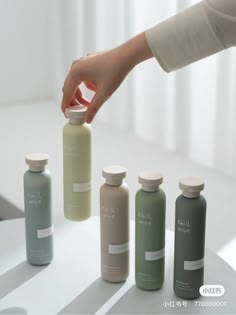 a hand reaching for an empty bottle next to three smaller bottles on a white table