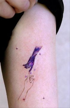 a woman's arm with a tattoo on it that has a purple bird flying through the sky