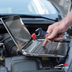 a man is working on his laptop under the hood of a car with a wrench