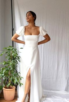 a woman in a white dress standing next to a plant