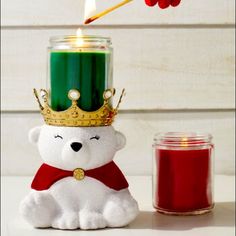 a white teddy bear sitting next to a candle with a crown on it's head