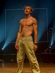 a shirtless man standing on top of a wooden floor in front of a stage