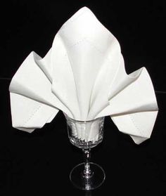 a white napkin folded over a wine glass on a black tableclothed surface,