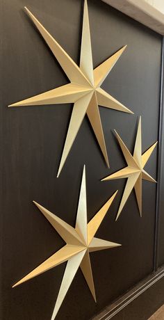 three paper stars hanging from the side of a black wall in front of a door