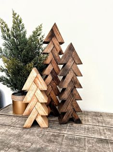 three wooden christmas trees sitting next to each other on top of a wood table near a potted plant