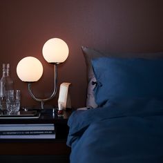 two lamps sitting on top of a night stand next to a bed with blue sheets