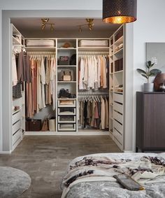 an open closet with clothes hanging on the walls and drawers, in front of a bed