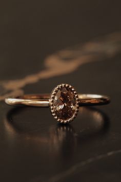 a gold ring with an oval shaped brown diamond in the center on a black surface