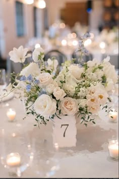 a vase filled with white and blue flowers on top of a table next to candles