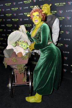 a woman in green dress pushing a baby carriage next to a man dressed as the grin