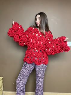 a woman is standing in front of a wall wearing red crocheted sweater and pants