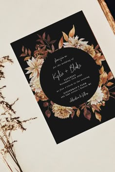 a black and white wedding card with floral designs on it, sitting next to dried flowers