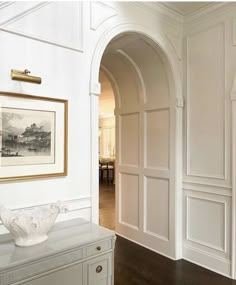 an archway leading to a living room with white walls and wood flooring, along with a painting on the wall