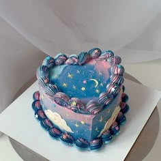 a blue heart shaped cake with stars and clouds on it's side, sitting on top of a white sheet