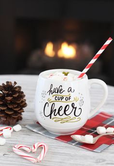 there is a cup of cheer with marshmallows and a pine cone on the table