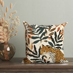 two pillows sitting on top of a wooden table next to vases with flowers and plants