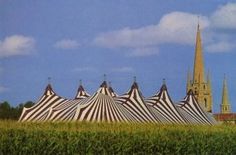 a row of striped tents sitting in the middle of a field next to a church