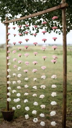 an outdoor ceremony with pink and white flowers hanging from the branches, in front of a green field