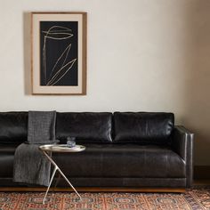 a living room with a black leather couch and coffee table in front of a painting