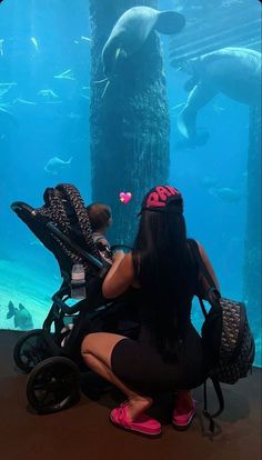 a woman sitting next to a baby in a stroller looking at an animal tank