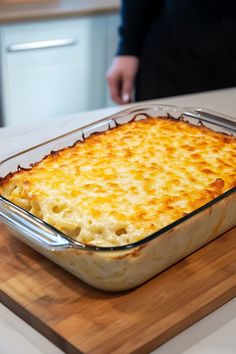 a casserole dish on a wooden cutting board with a person in the background