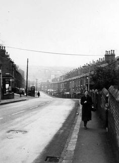 an old black and white photo of a woman walking down the street with buildings in the background