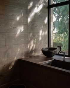 a sink sitting under a window next to a wooden counter with a bowl on it