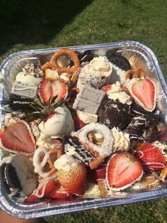 a container filled with assorted desserts on top of a grass covered field next to a person