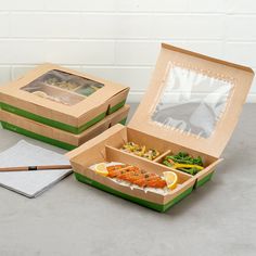 two boxes with food inside sitting on a table next to a notepad and pencil