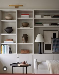 a living room filled with lots of white bookshelves next to a table and chair