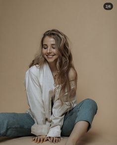 a woman sitting on the floor with her hands in her pockets and smiling at the camera