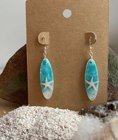 a pair of earrings with starfish and turquoise stone on them sitting in front of a cardboard box