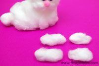 a small white cat sitting on top of a pink surface next to some fluffy clouds