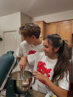 two people in the kitchen making something to eat and smile at each other as they stand next to an electric mixer